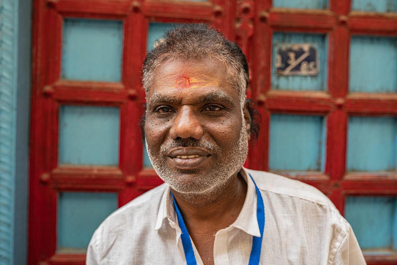 Close-up portrait of a smiling man in Varanasi, India surrounded by colorful architecture.
